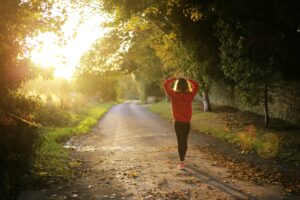 A woman in a red hoodie walks away down a sunlit autumn path